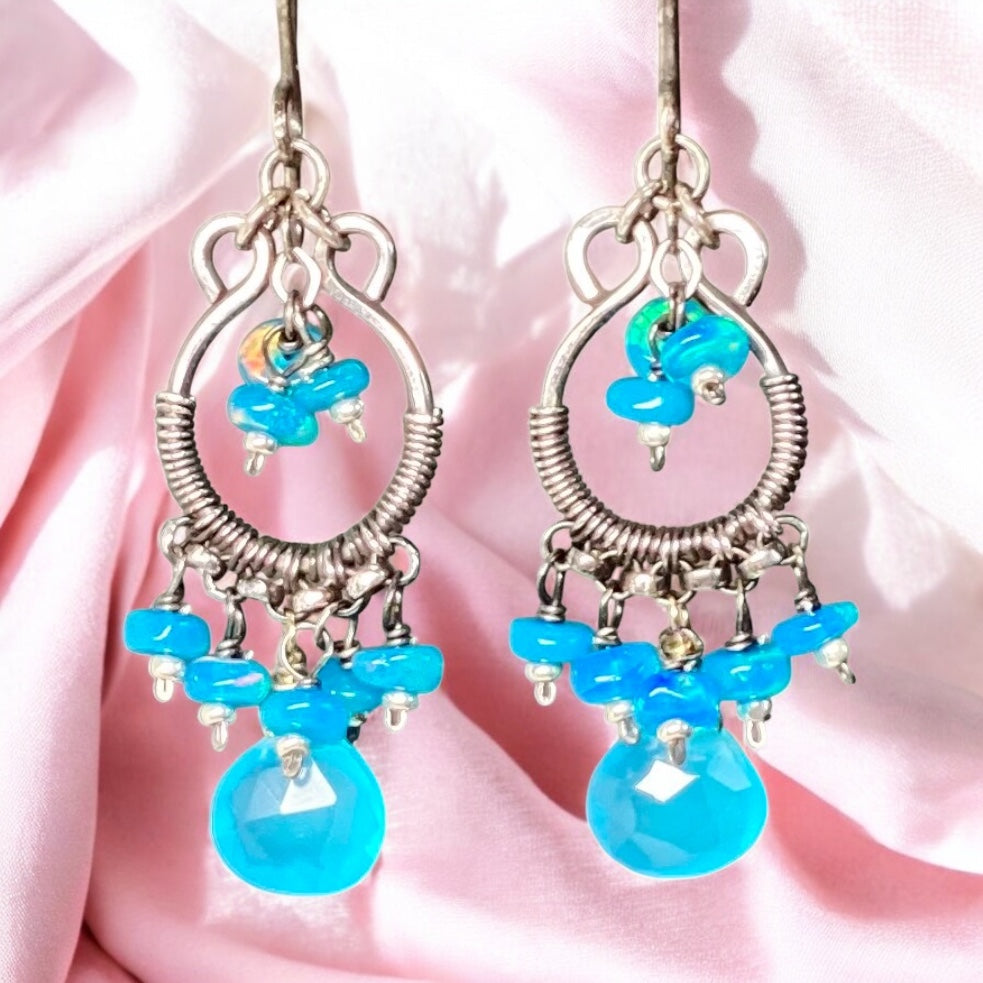 Pair of earrings with blue beads and silver hooks on a pink fabric background