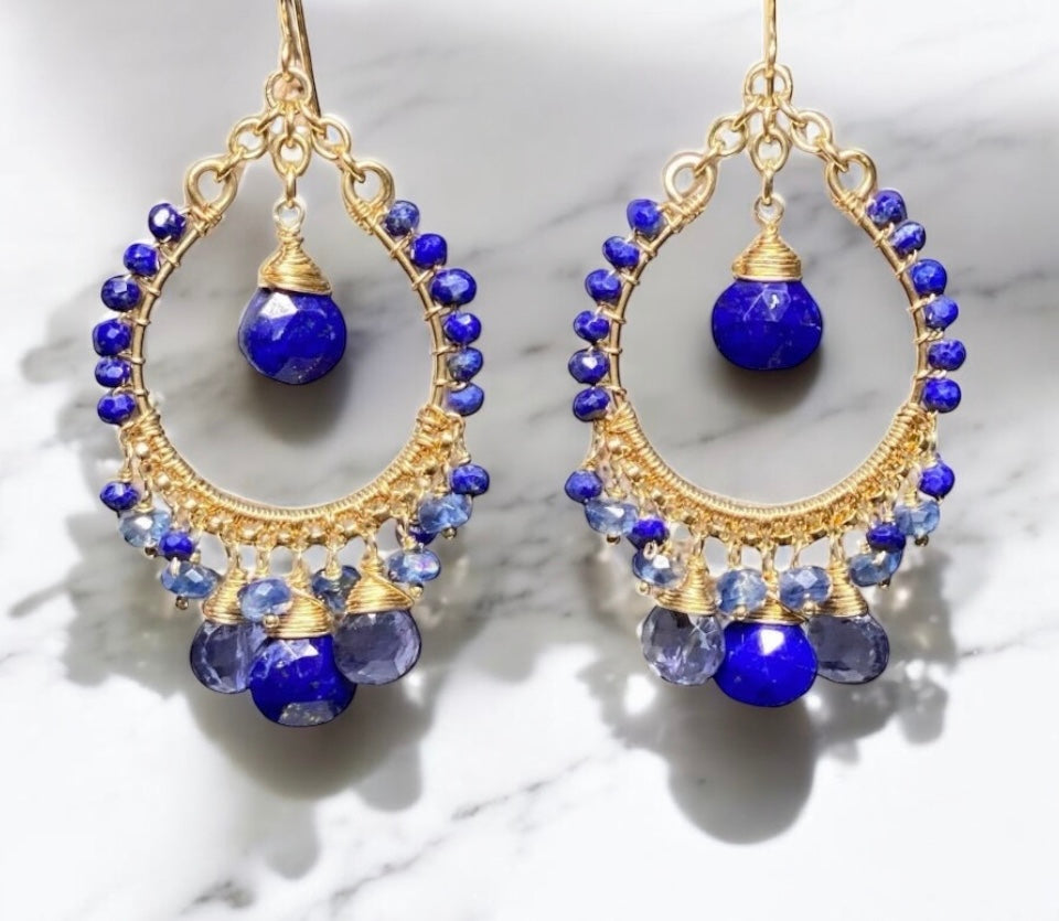 Gold hoop earrings with blue gemstones on a marble background