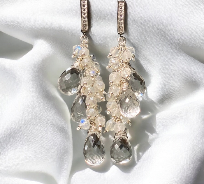 Delicate earrings with clear gemstones on a white fabric background