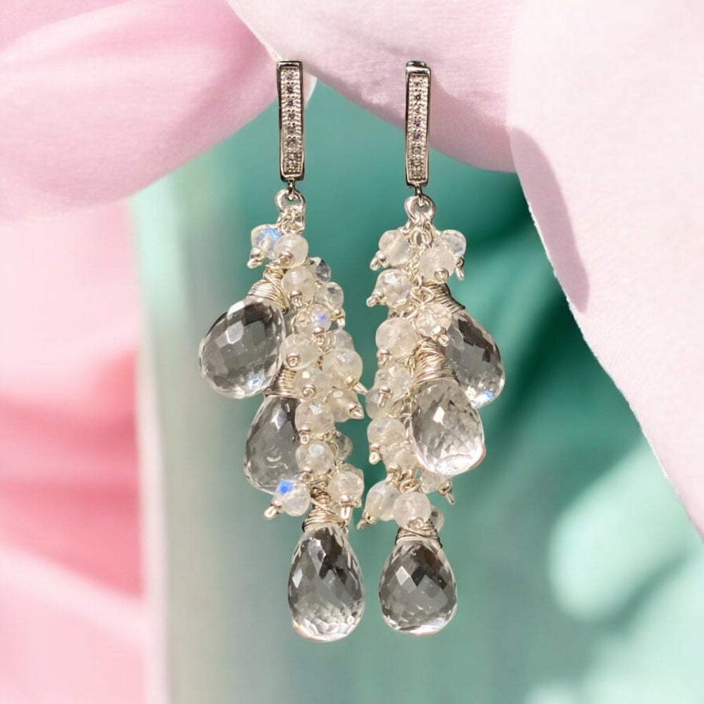 Delicate earrings with gemstones against a soft pink and green background