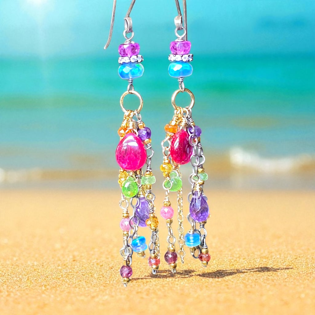 Colorful beaded earrings on a beach with turquoise water and sand in the background