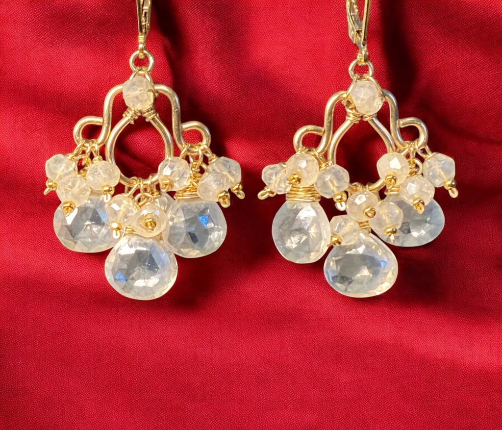Gold chandelier earrings with clear gemstones on a red background