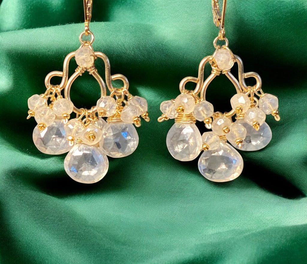 Gold chandelier earrings with clear gemstones on a green fabric background