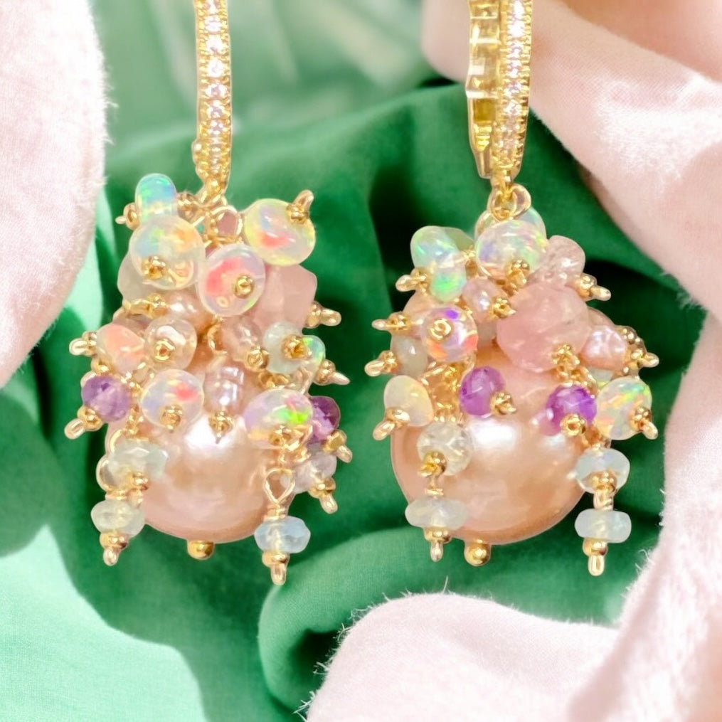 Ornate earrings with pink and gold details held by a hand against a green background