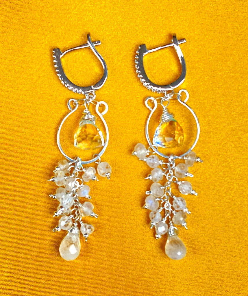 Rainbow quartz and moonstone earrings with lever-back closures, silver hoop forms and dangling gemstone tassels on yellow fabric.