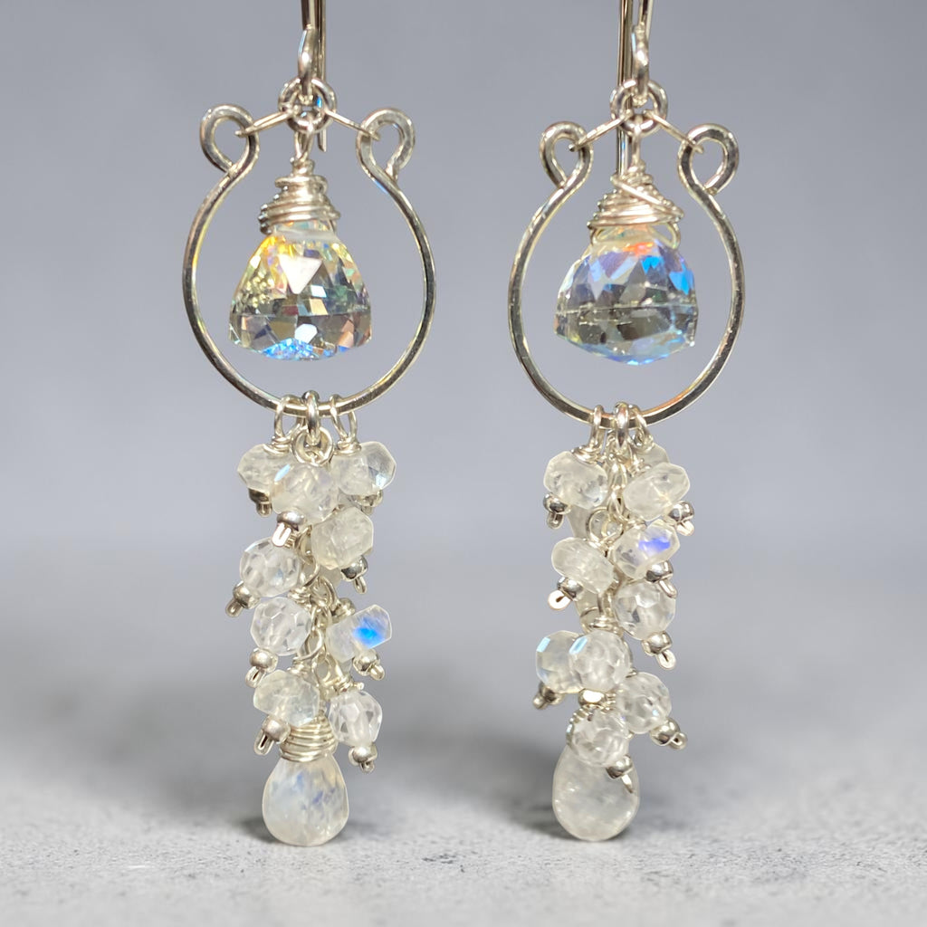 Pair of sterling silver earrings with mystic crystal and moonstones on a gray background.