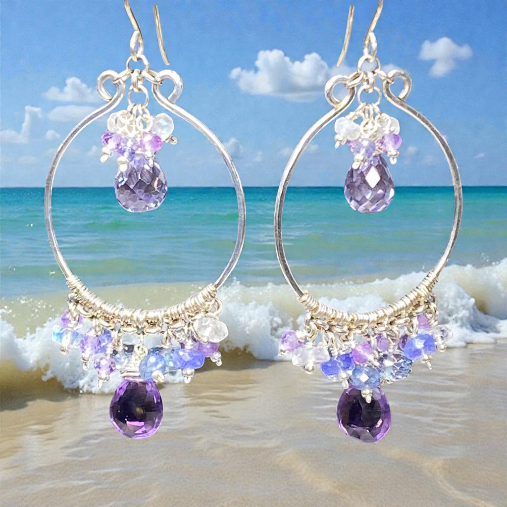 Colorful gemstone chandelier earrings amethyst tanzanite blue violet quartz dangling over beach surf waves and blue sky