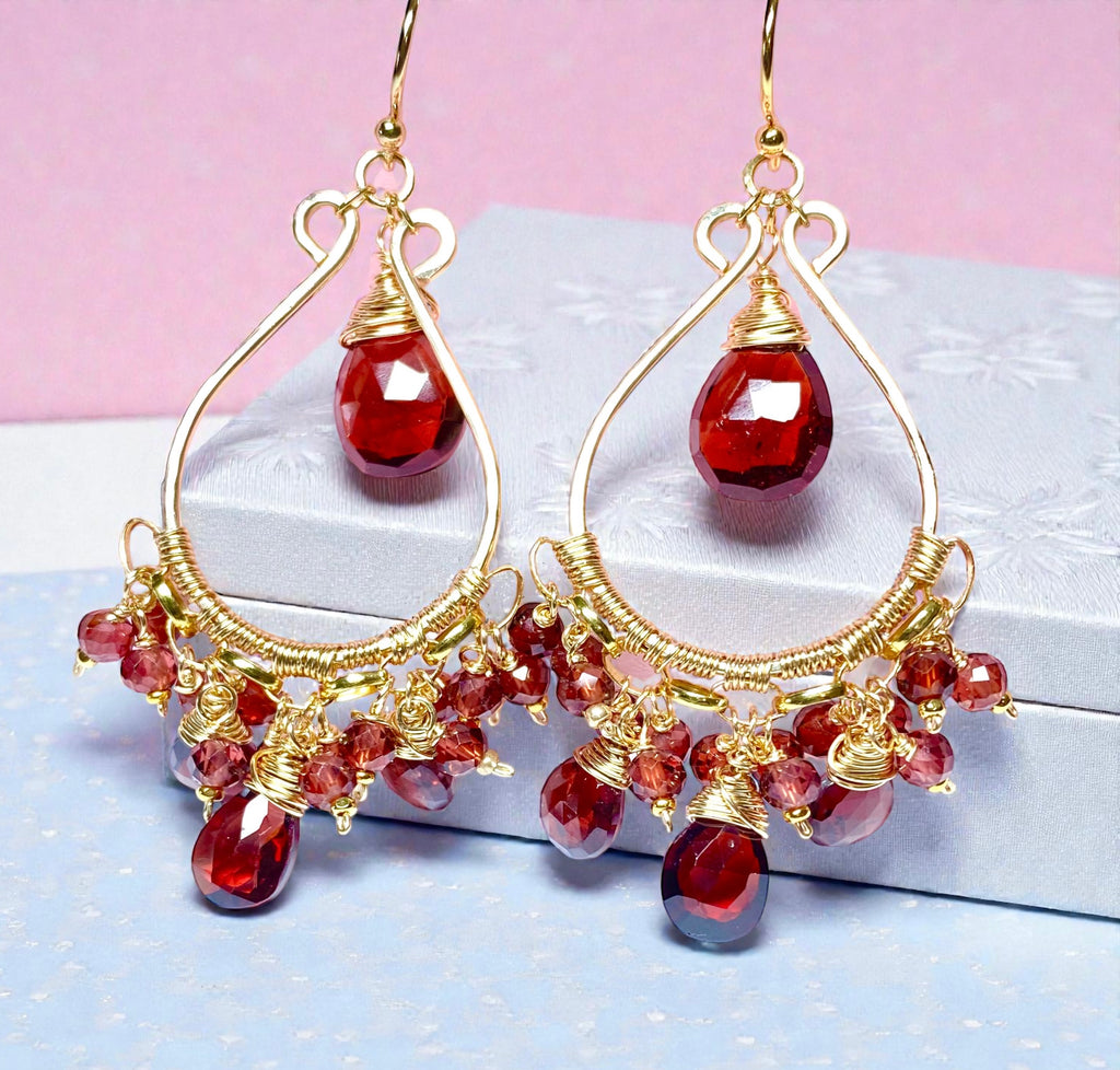 Red garnet chandelier earrings 14kt gold fill leaning against white jewelry box in front of pink background