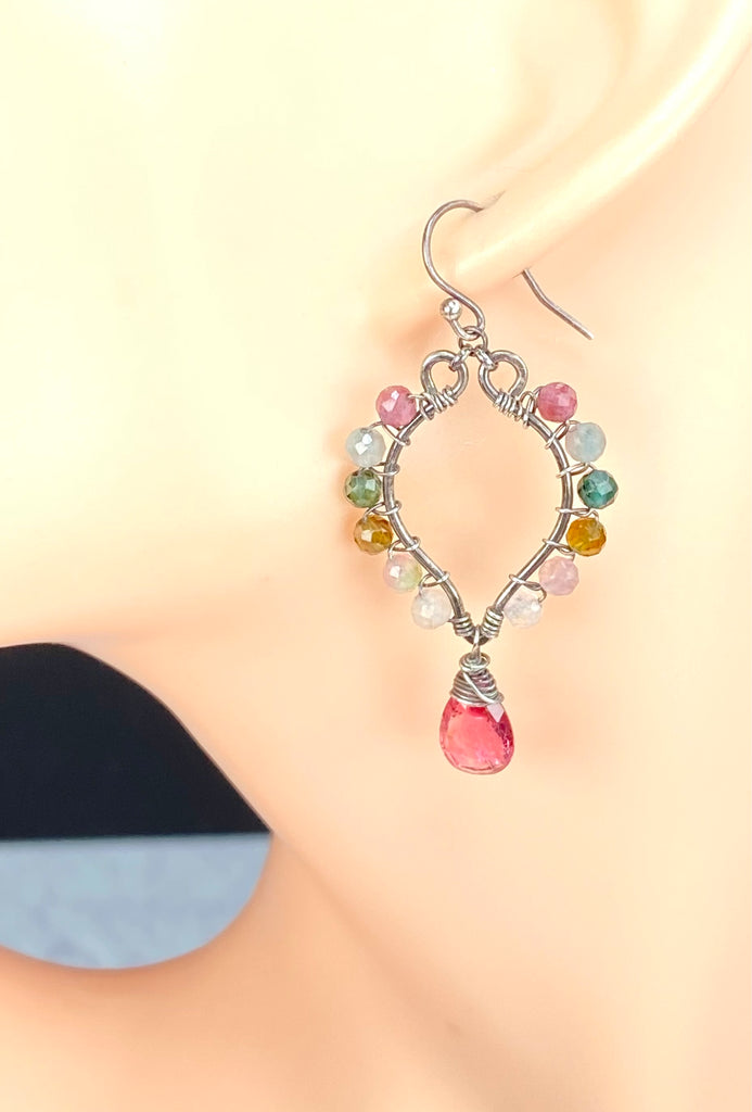 A single dangling hoop earring displayed on a model's ear. The earring has an oxidized sterling silver-tone wire frame with small multicolored tourmaline gemstone beads around the top half and a faceted pink teardrop tourmaline gemstone hanging from the bottom.