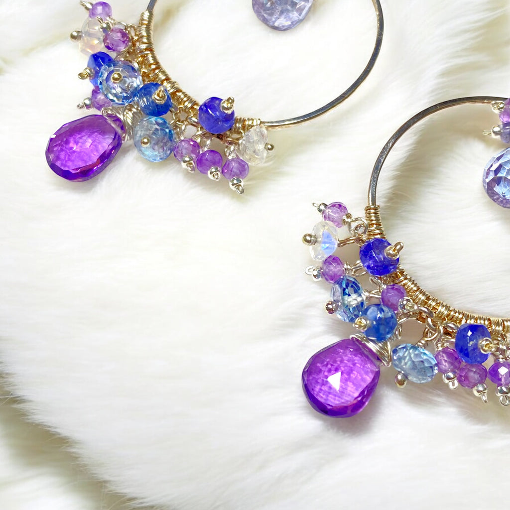 Colorful gemstone chandelier earrings amethyst tanzanite blue violet quartz closeup of bottom clusters on white furry fabric