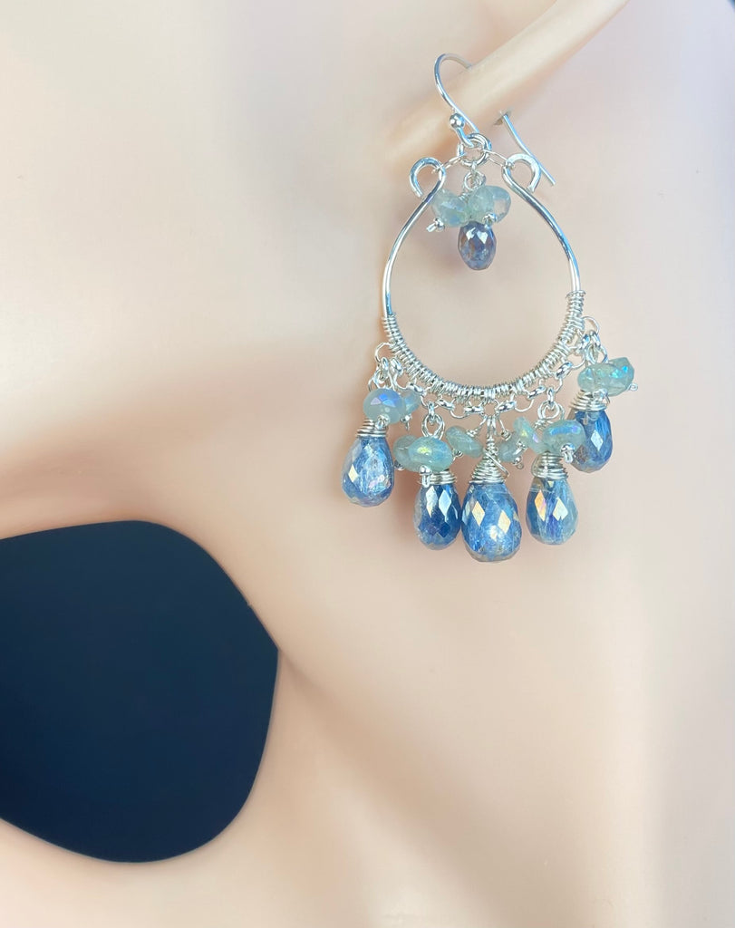 A pair of sterling silver chandelier hoop earrings with dangling blue faceted beads, displayed on a femalie mannequin ear.