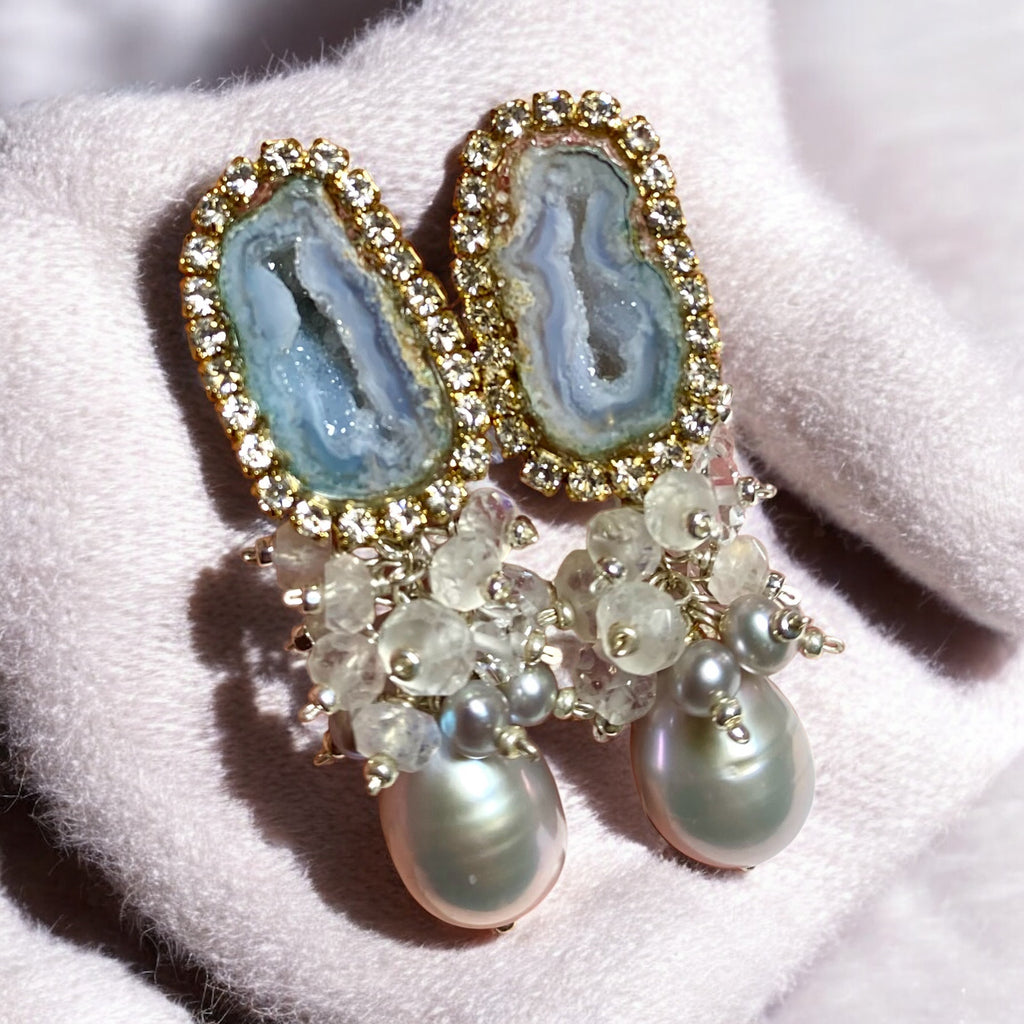 Elegant earrings with gemstones and pearls on a grey surface