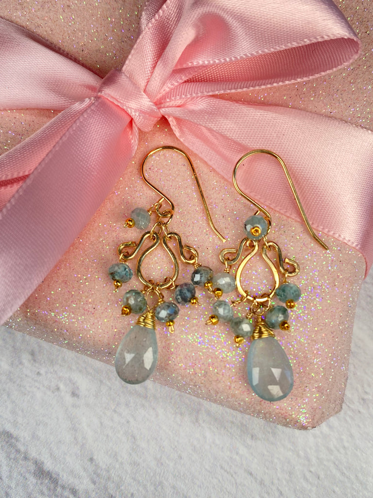 Moss aquamarine and blue zircon gold-filled chandelier earrings resting on a sparkling pink gift box beneath a pink satin bow.