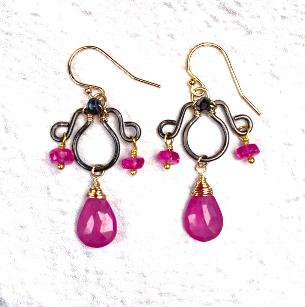 Mixed-metal pink sapphire chandelier earrings on white, showing gold-filled French hooks, blackened silver frames and gold-wrapped sapphire pear drops.
