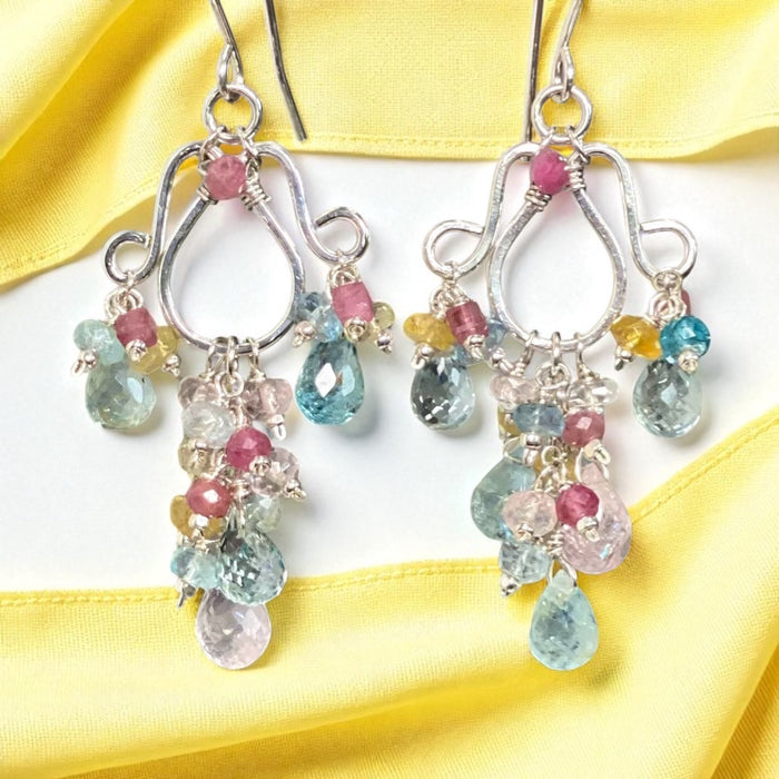 Multicolor aquamarine and pink tourmaline sterling silver chandelier earrings with blue pink yellow gemstones dangling in front of yellow and white silk fabrics