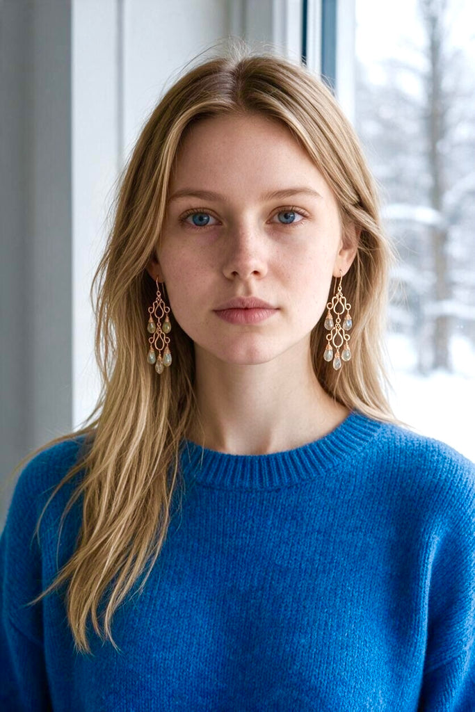 Model in a blue sweater wearing double labradorite chandelier earrings in rose gold fill beside a window.