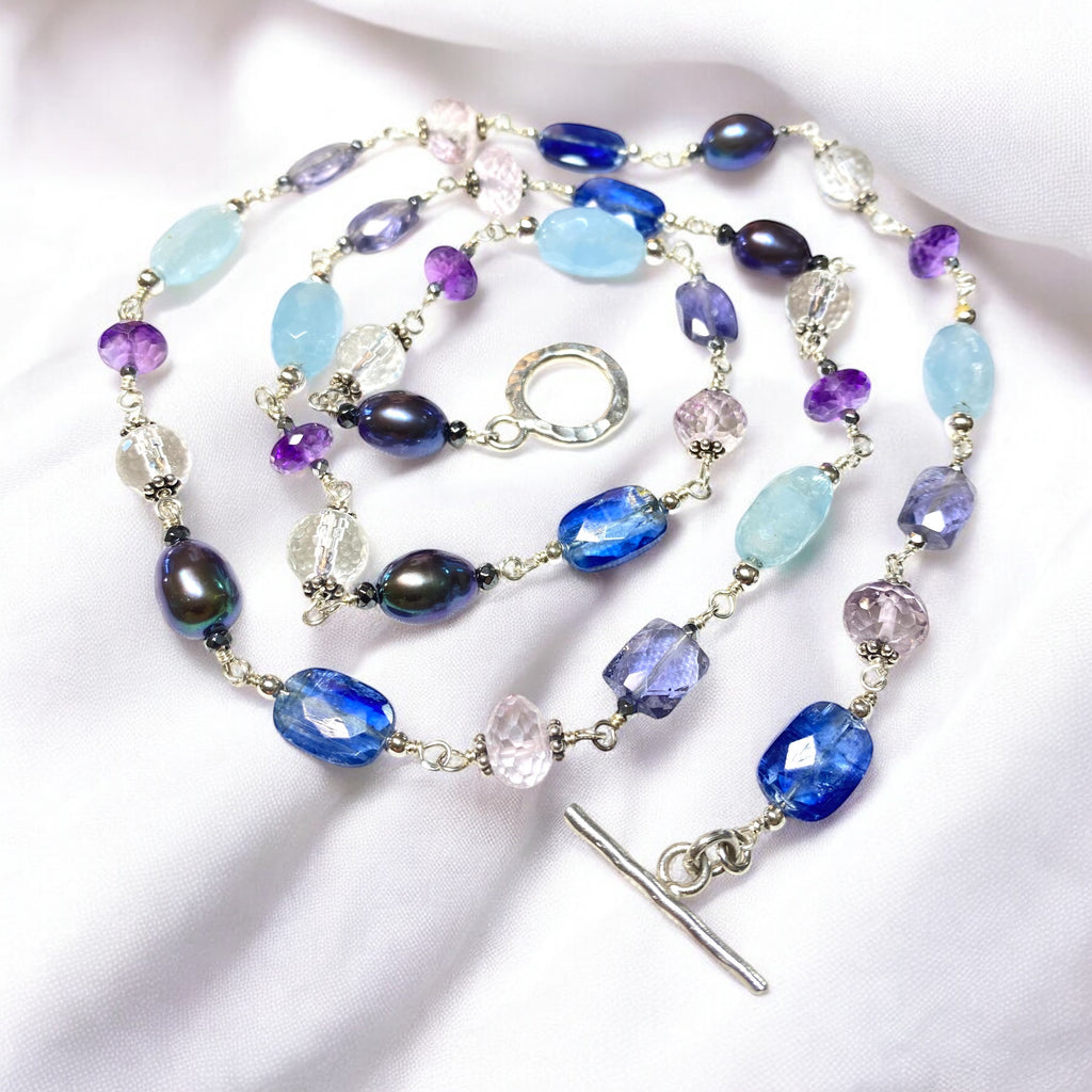 Blue purple gemstone peacock pearl long necklace sterling silver lying flat in circle on draped white fabric