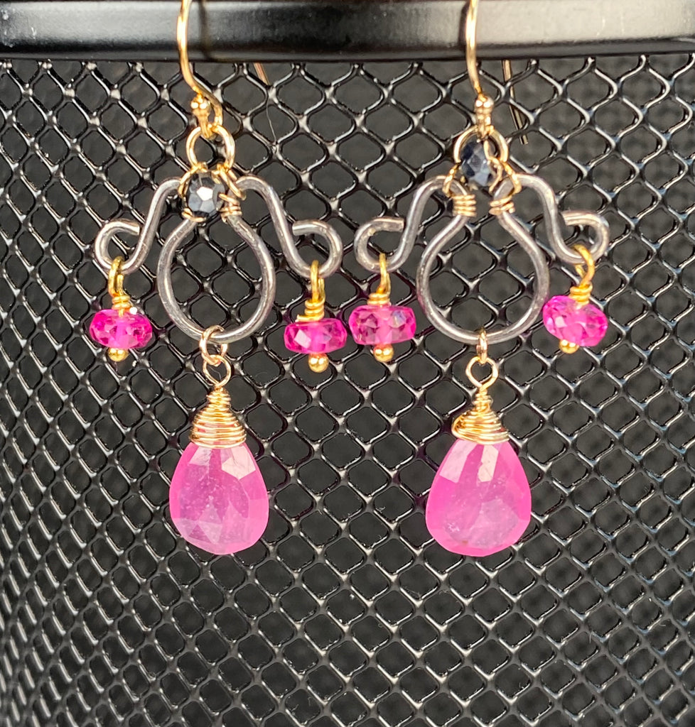 Pink sapphire chandelier earrings hanging on black mesh, with faceted pear drops, fuchsia sapphire side accents and mystic black spinel at the tops.