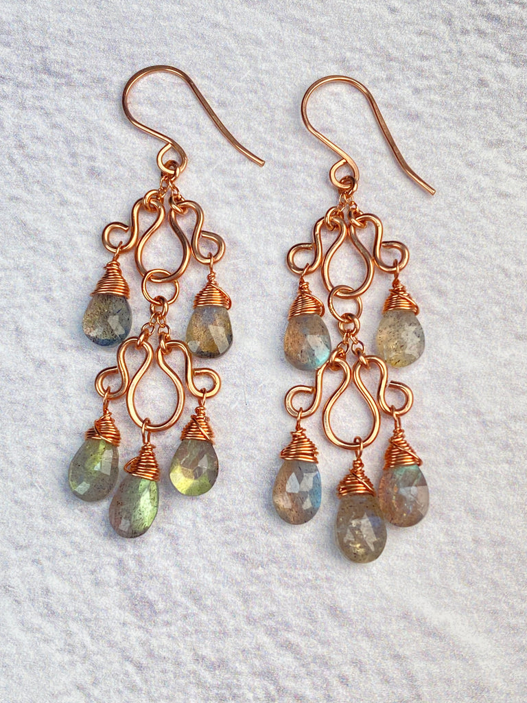 Pair of double-tier labradorite chandelier earrings resting on white fabric, showing French hooks, curled rose gold-filled frames, and faceted gemstone drops.