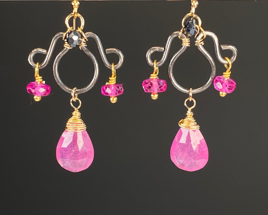 Front view of pink sapphire chandelier earrings against black, with fuchsia rondelles, mystic black spinel and contrasting silver and gold wirework.