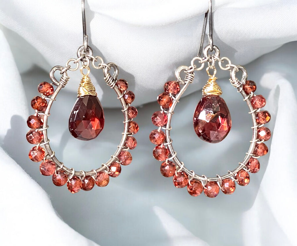 Red garnet hoop earrings mixed metals oxidized sterling silver and 14kt gold fill dangling in front of bright white draped fabric