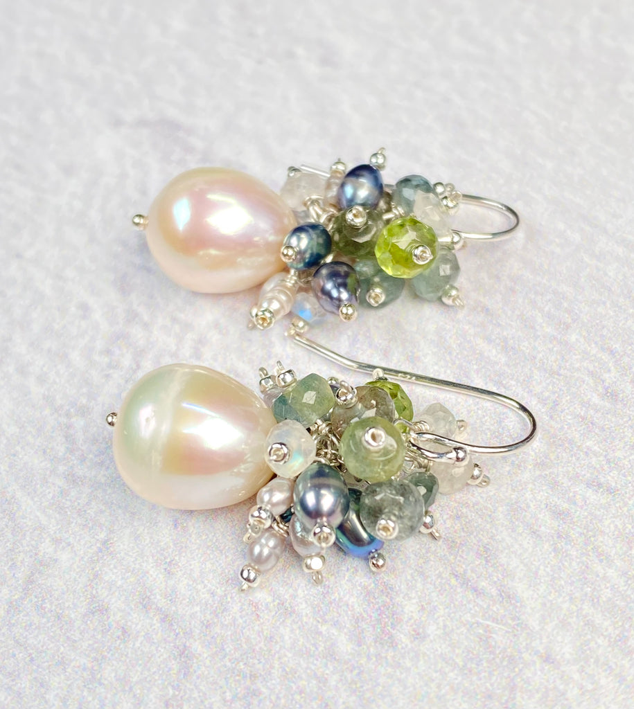  wider view: Pair of sterling silver cluster earrings on a white background, featuring ivory freshwater baroque pearl drops beneath moss aquamarine, peridot, rainbow moonstone and peacock pearl clusters.