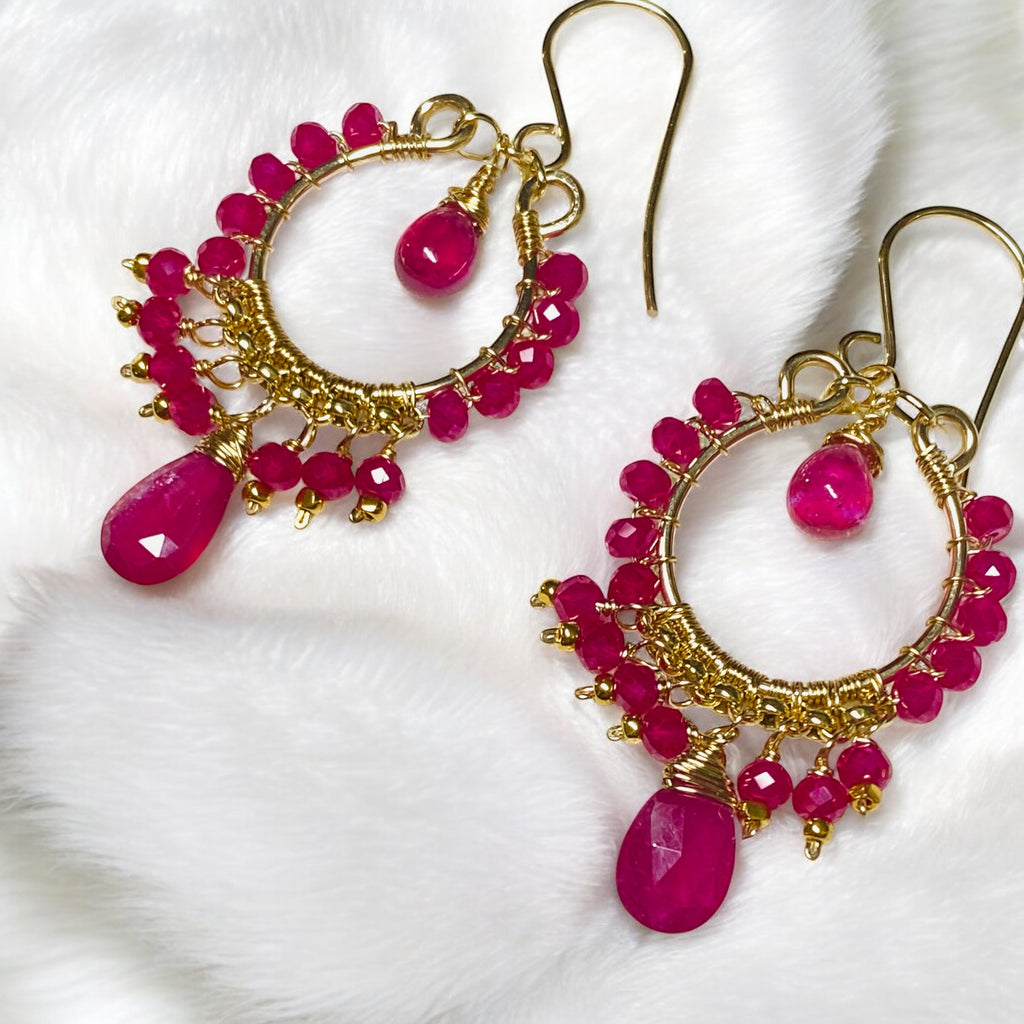 Red ruby pink sapphire gold chandelier hoop earrings laying on white furry fabric