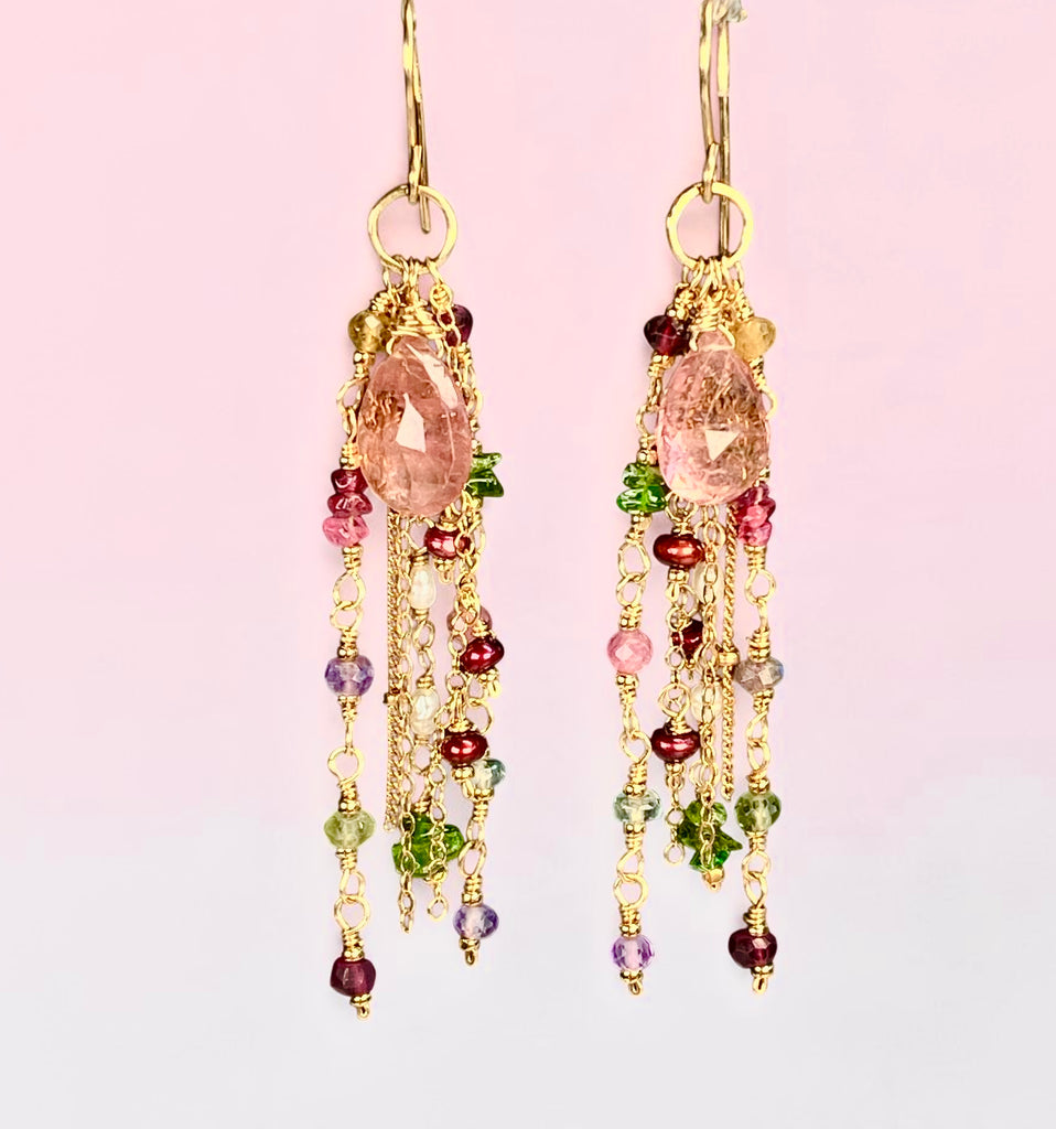 Pink tourmaline gold-filled dangle earrings against a pale pink background, featuring large faceted pink drops, green chrome diopside and colorful gemstone and pearl accents.