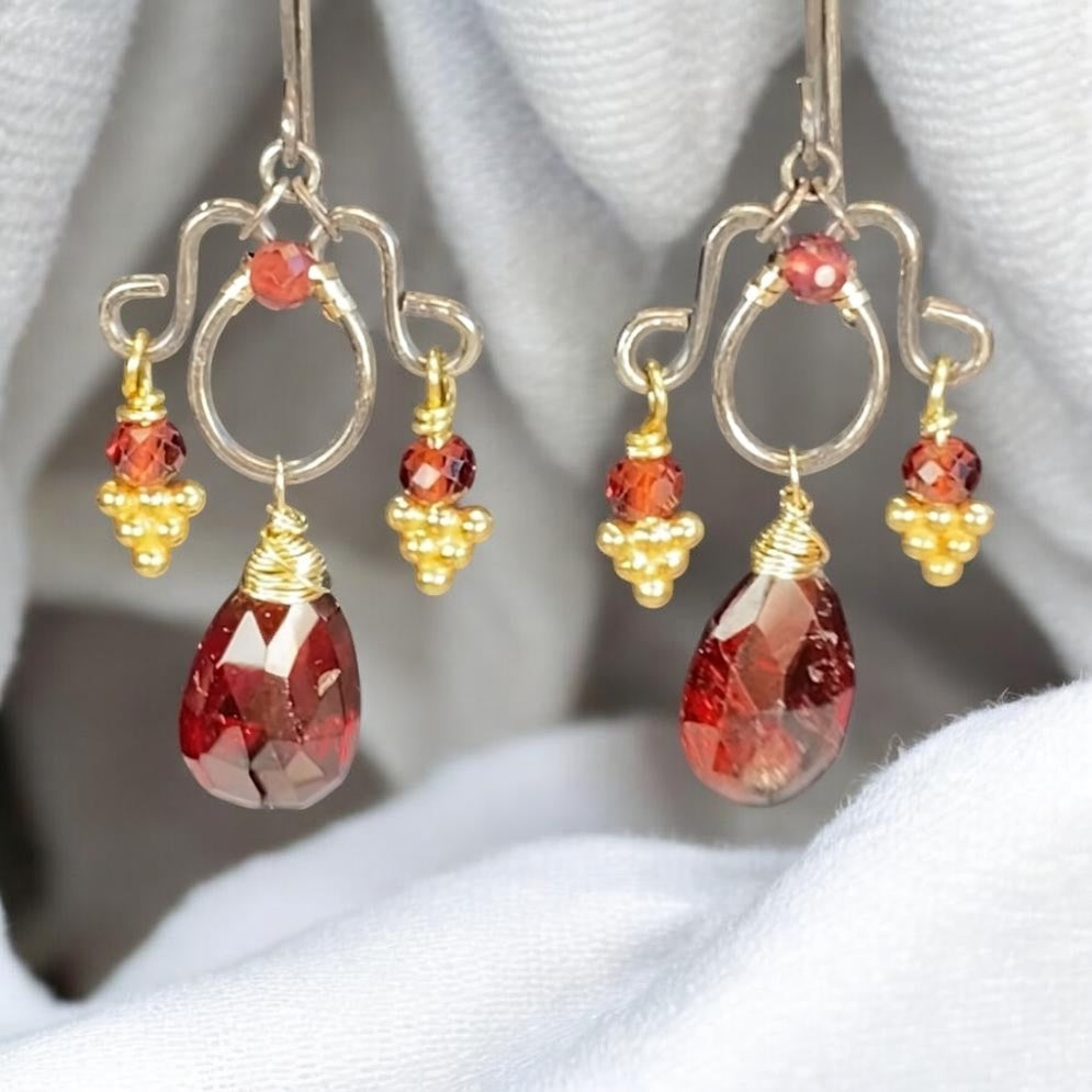 Mixed-metal garnet chandelier earrings suspended against white fabric, with red gemstone drops and vintage gold vermeil headpin details.