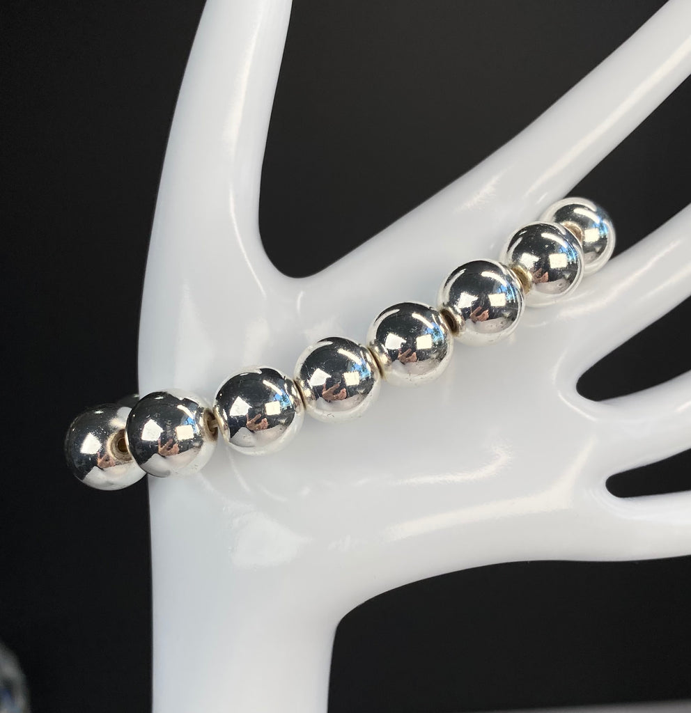 Silver hematite stretch bracelet draped diagonally across a white display hand against a dark background, showing the smooth round beads.