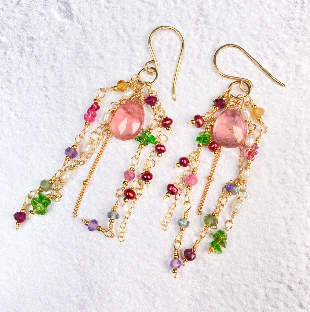 Pink tourmaline earrings laid on textured white fabric, showing hand-wrapped gold-filled French hooks, large pink briolettes and cascading gemstone and pearl chains