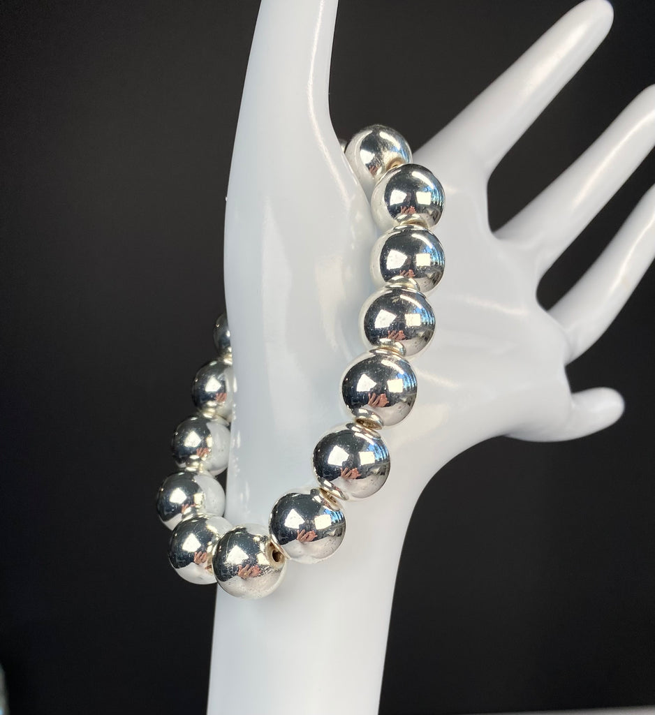 Silver hematite stretch bracelet curved around a white display hand against a dark background, highlighting the polished 12 mm beads.