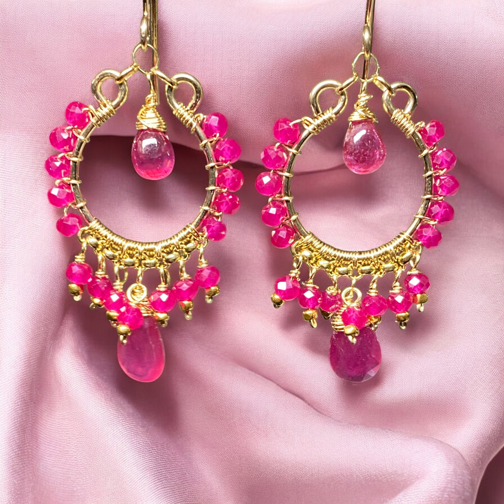 Red ruby pink sapphire gold chandelier hoop earrings dangling in front of pink draped fabric
