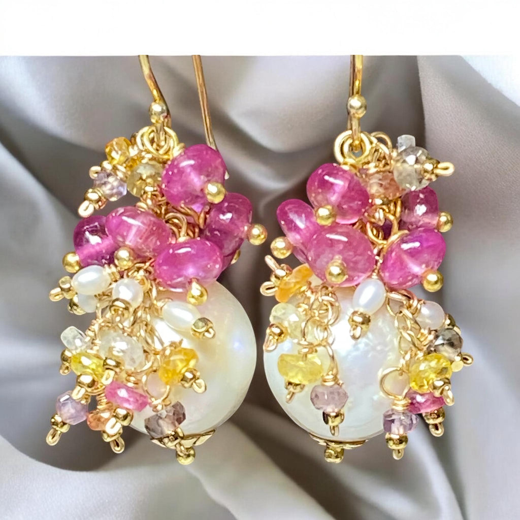Pearl and pink sapphire cluster earrings gold dangling in front of draped grey fabric background