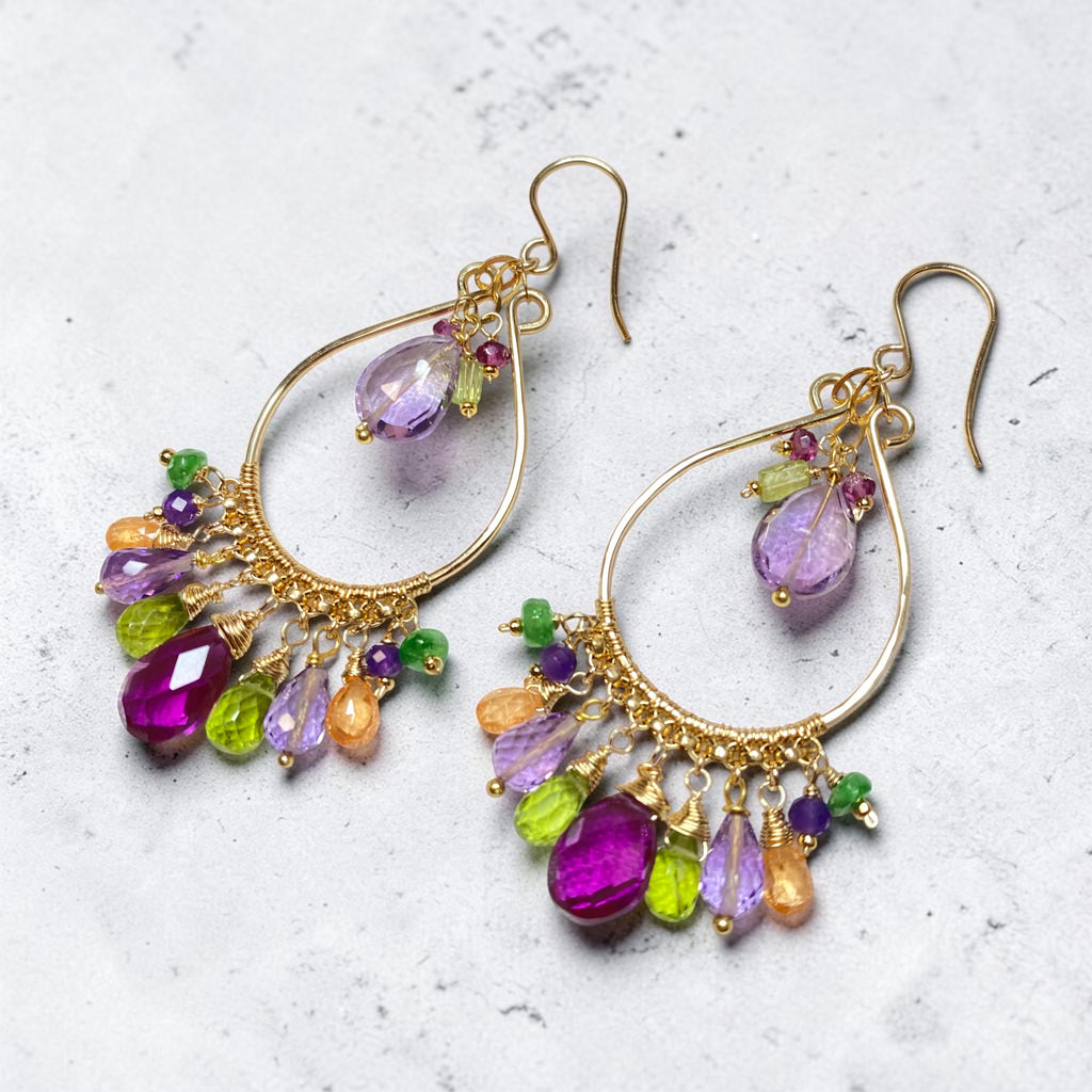 Colorful gemstone chandelier hoop earrings lying on grey and white marble — violet quartz, peridot, amethyst, mandarin garnet, gold fill