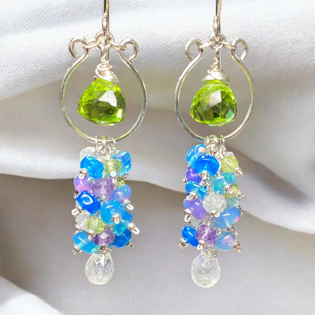 Natural peridot and rainbow moonstone teardrop briolettes on sterling silver chandelier hoop earrings against draped white fabric background