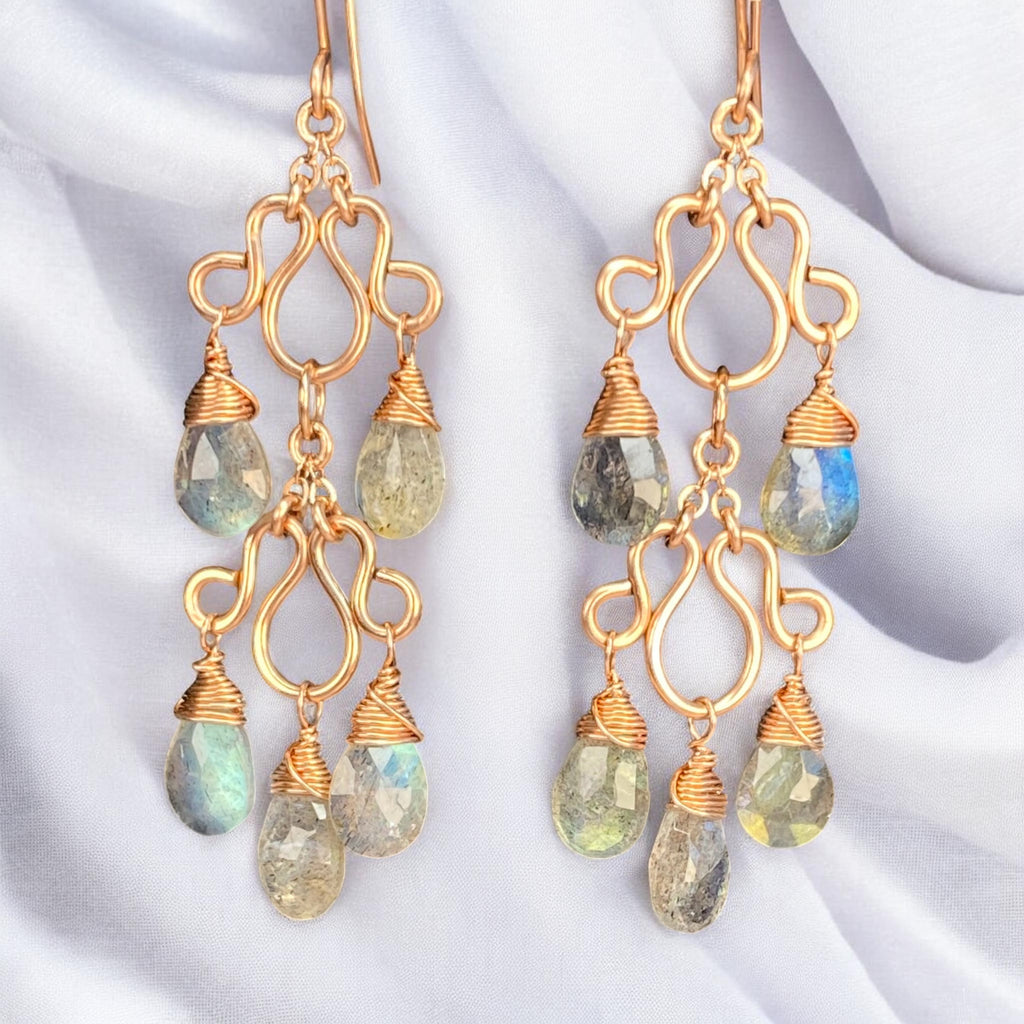 Double labradorite chandelier earrings against draped white fabric, with rosy wirework and blue, green, and pale gold gemstone flashes.