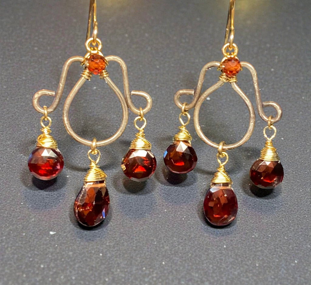Oxidized silver chandelier earrings dangling red garnet faceted briolettes wire wrapped in 14kt gold fill wires shown in front of a grey background.