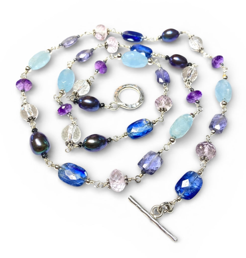 Blue purple gemstone peacock pearl long necklace sterling silver lying flat in concentric circle on plain white background