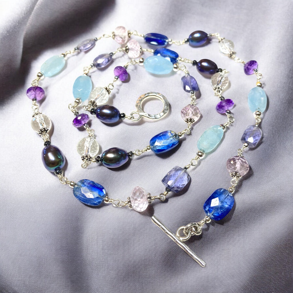 Blue purple gemstone peacock pearl long necklace sterling silver lying flat in concentric circle on draped grey fabric