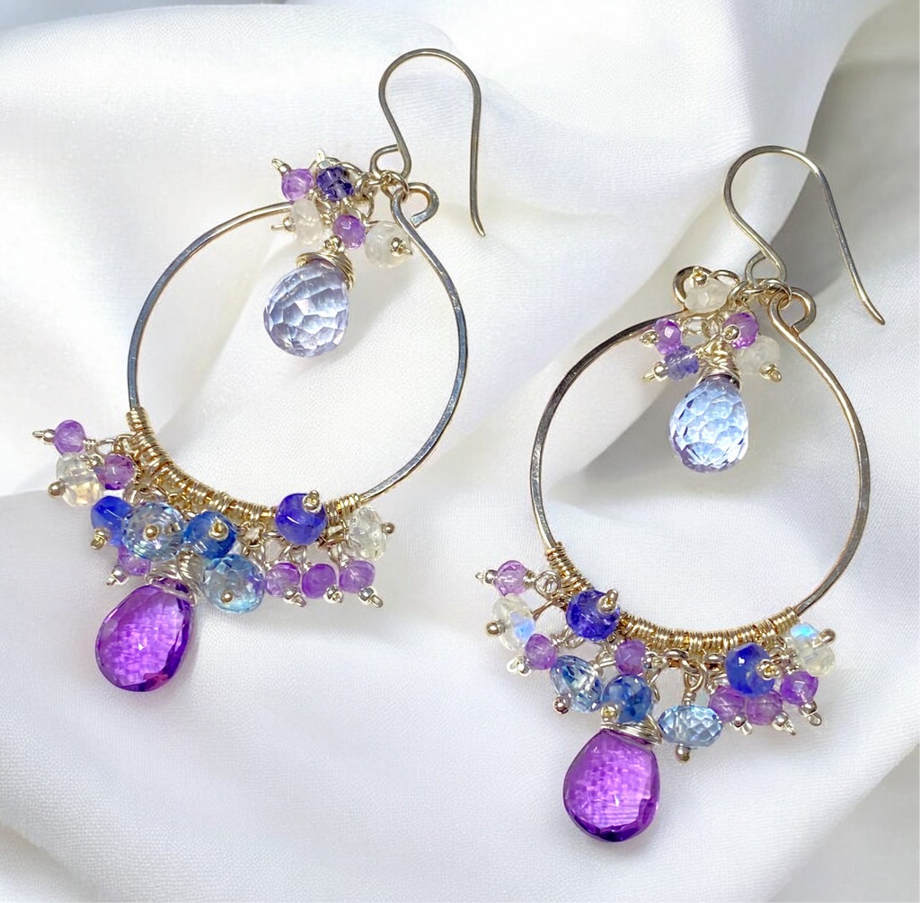 Colorful gemstone chandelier earrings amethyst tanzanite blue violet quartz lying on bright white draped fabric