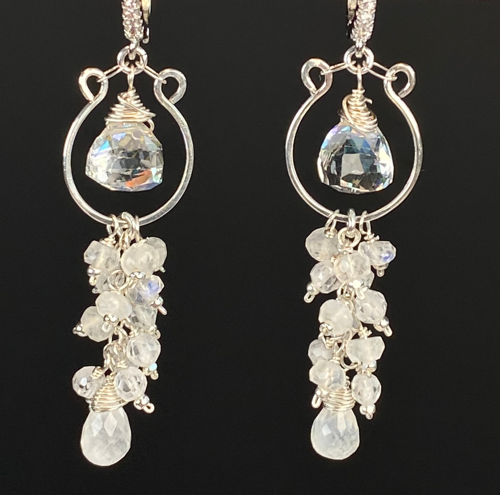 Close-up of rainbow quartz trillions suspended inside silver hoops above moonstone and white zircon tassels, shown with lever-back closures.