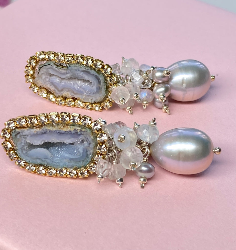 Pair of earrings with geode and pearl designs on a pink background