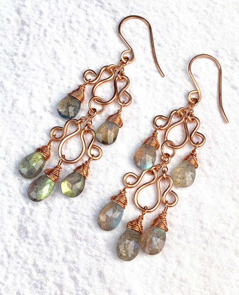 Double labradorite chandelier earrings lying diagonally on white textured fabric, showing rose gold-filled French hooks and wirework.