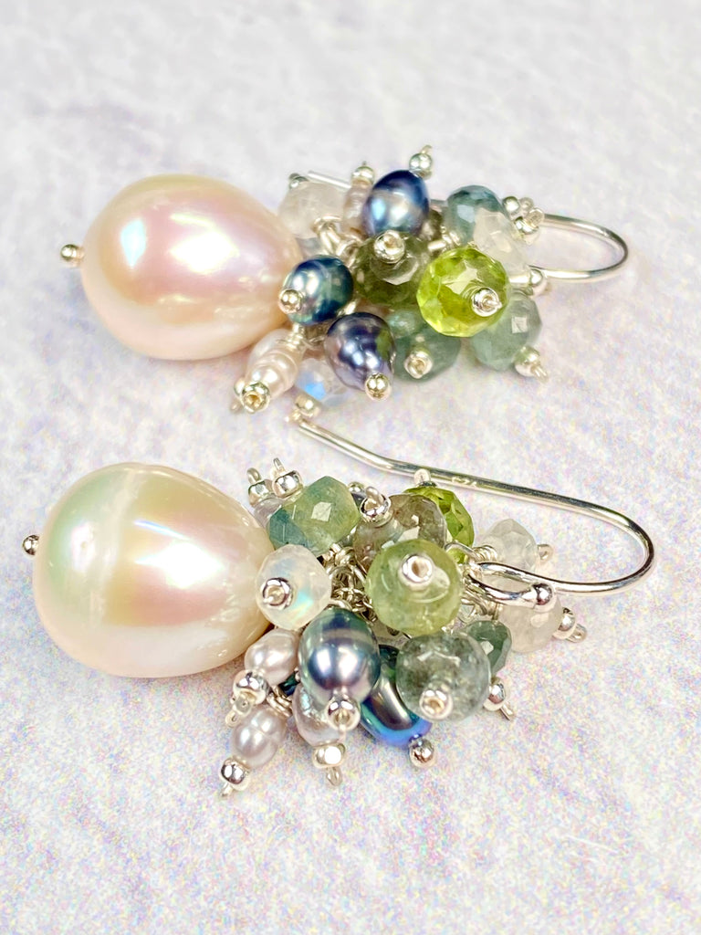 tighter close-up: Moss aquamarine and freshwater baroque pearl cluster earrings with green peridot, rainbow moonstone and blue peacock pearls, wire wrapped in sterling silver with French hooks on a white background.