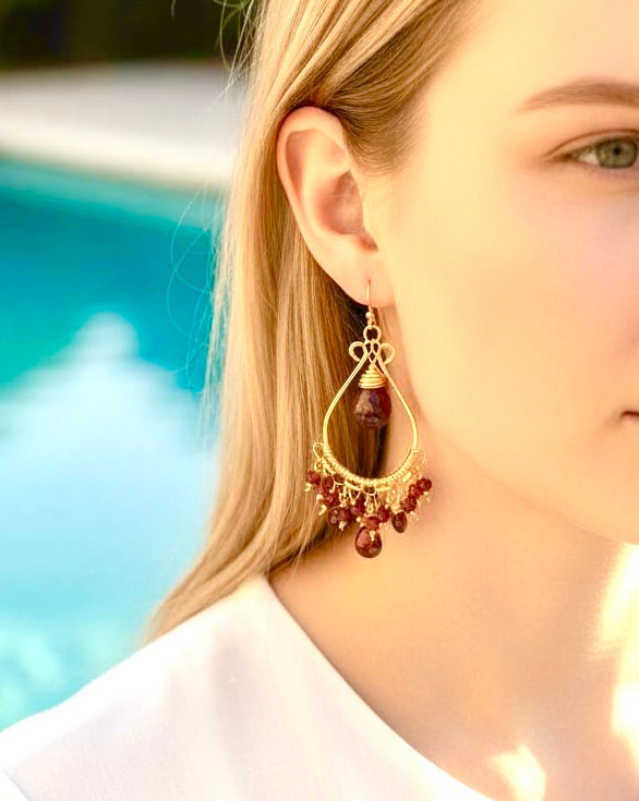 Red garnet chandelier earrings 14kt gold fill closeup on model's ear in front of pool