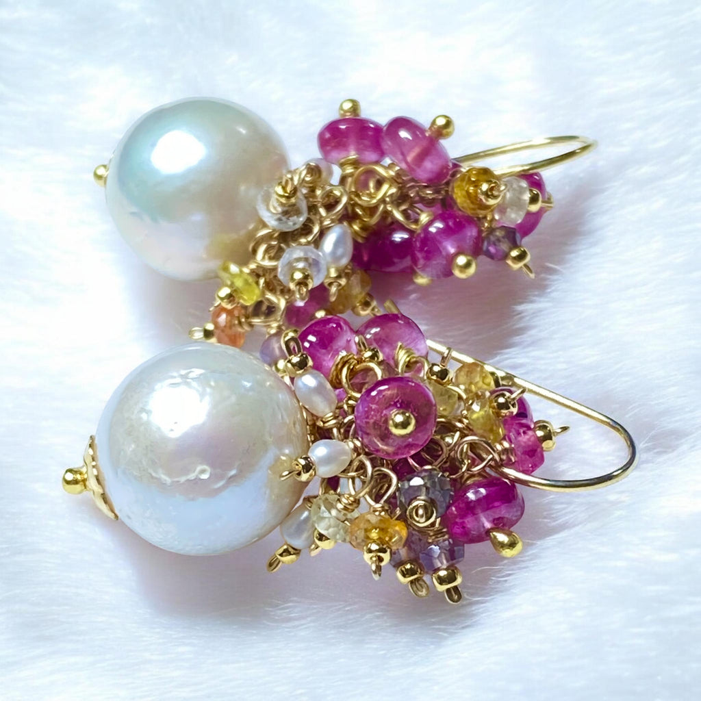 Pearl and pink sapphire cluster earrings gold lying on white furry fabric - flat lay showing rainbow sapphire detail