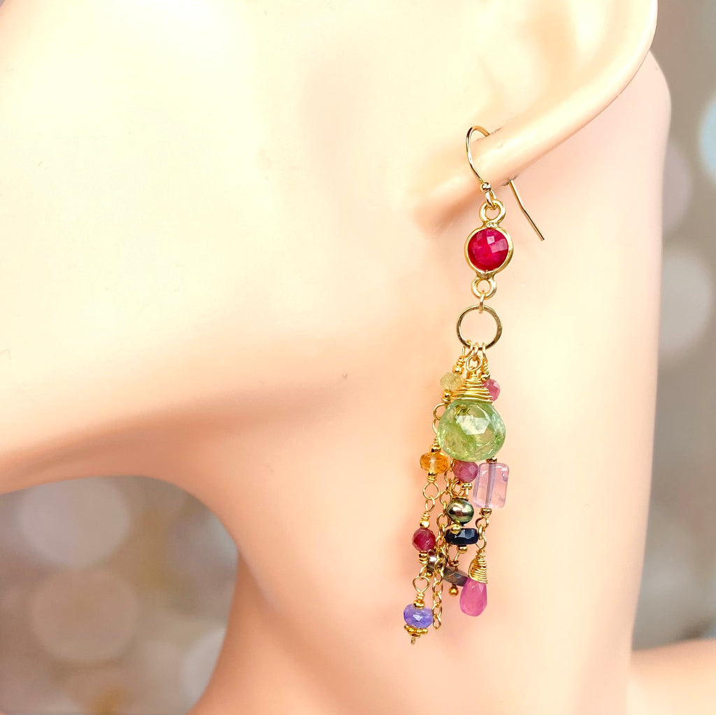 A gold-toned dangle earring with a bright pink round bead, a faceted green bead, and multiple dangling multicolored beads, shown on a mannequin ear.