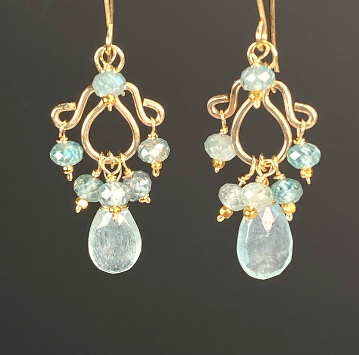  hanging against dark background:
Moss aquamarine and blue zircon petite chandelier earrings in 14kt gold fill, with open scrollwork, blue bead accents and faceted aquamarine drops against a dark background.