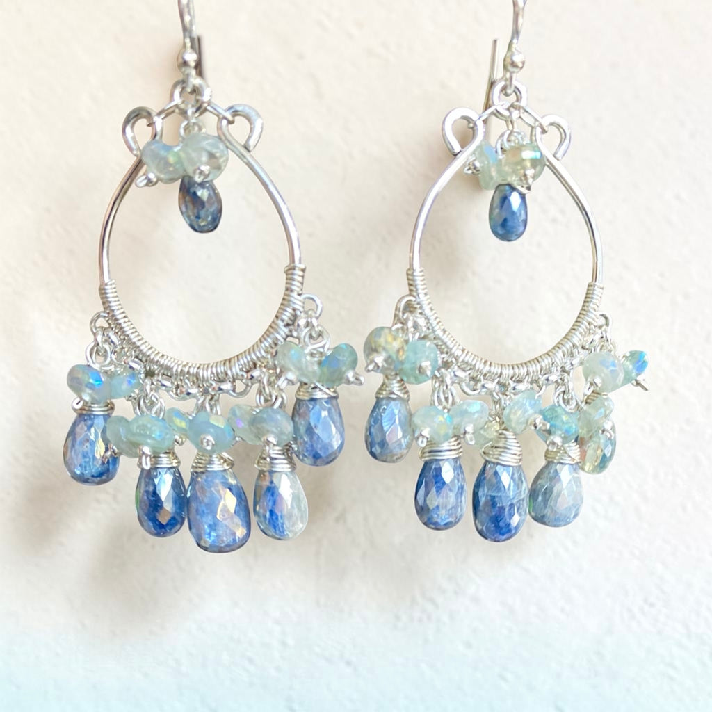 A pair of sterling silver hoop chandelier earrings with faceted blue teardrop beads and iridescent light blue beads, shown against a plain off-white background.